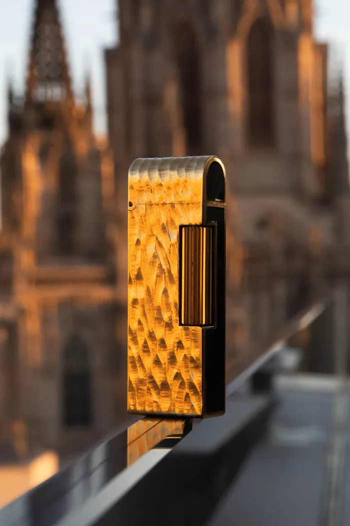 Gold Dunhill Rollagas lighter with a dome top, in front of Barcelona cathedral at sunset
