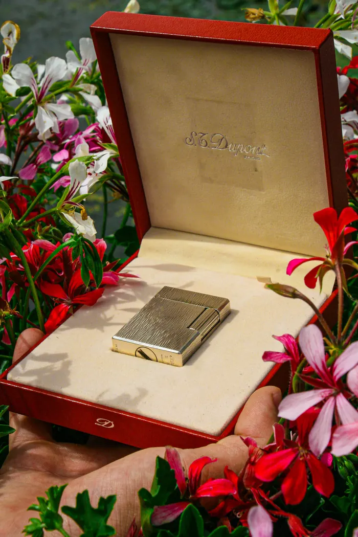 S.T. Dupont Ligne 1 small lighter in its red box, held among geraniums